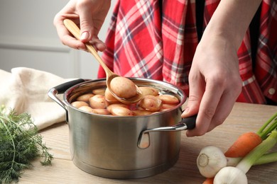 Woman taking raw potato from pot with water at wooden table, closeup