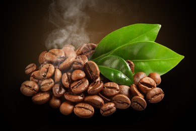 Freshly roasted coffee beans and green leaves on dark background