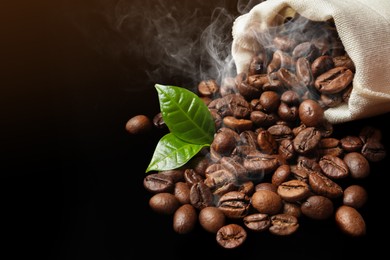 Freshly roasted coffee beans and green leaves on dark background
