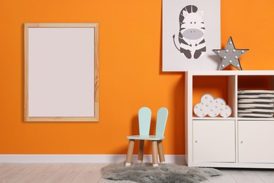 Room for child with empty picture frame on orange wall. Interior design