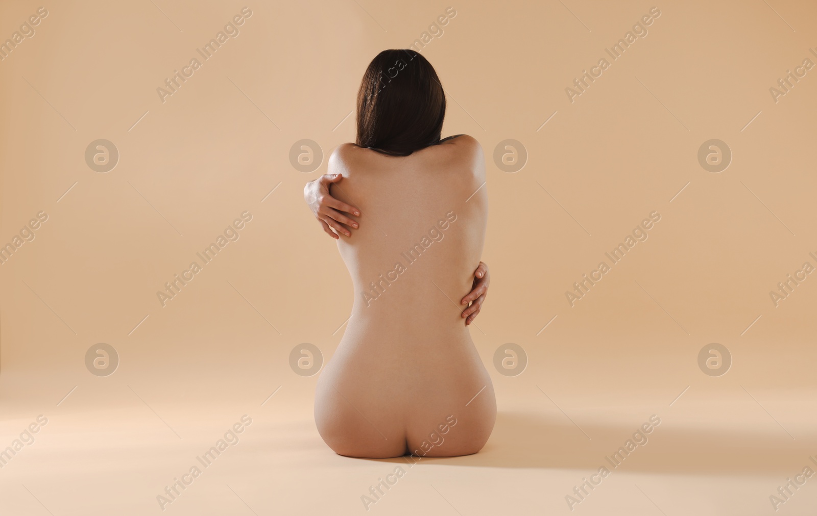 Photo of Nude woman on beige background, back view
