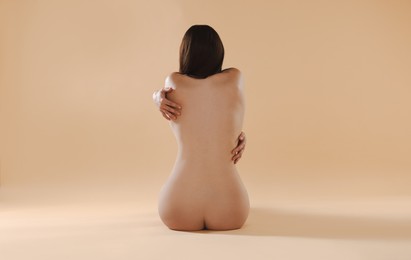 Nude woman on beige background, back view