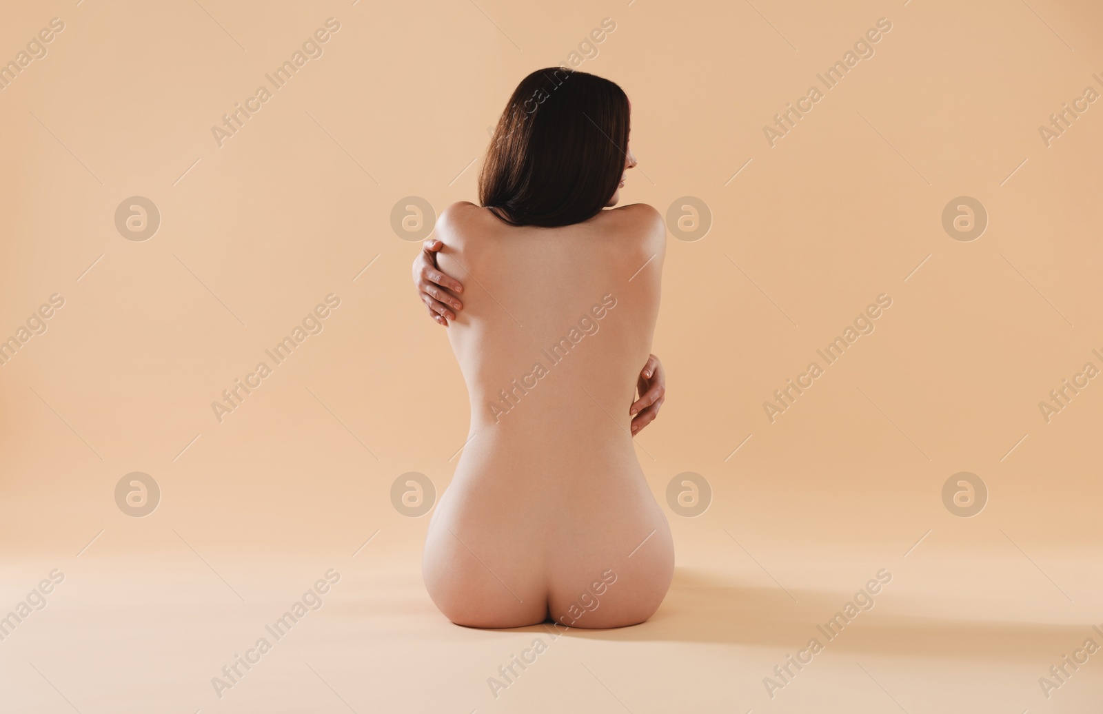 Photo of Nude woman on beige background, back view