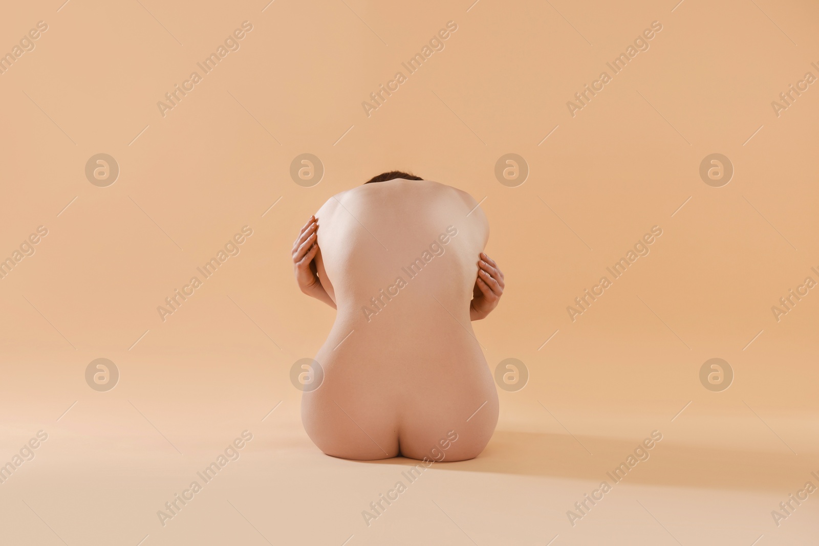 Photo of Nude woman on beige background, back view