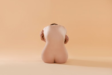 Photo of Nude woman on beige background, back view