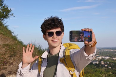 Travel blogger in sunglasses with smartphone streaming outdoors