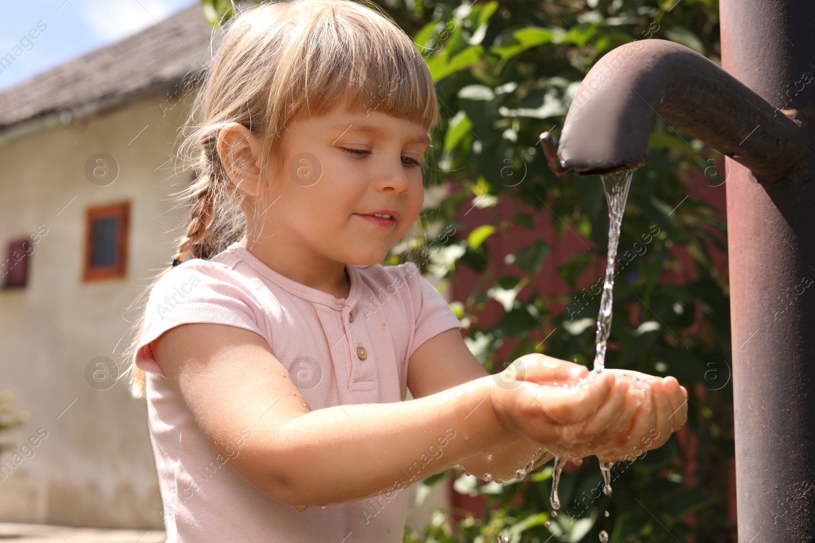 Photo of Water scarcity. Cute little girl drawing water with hands from tap outdoors