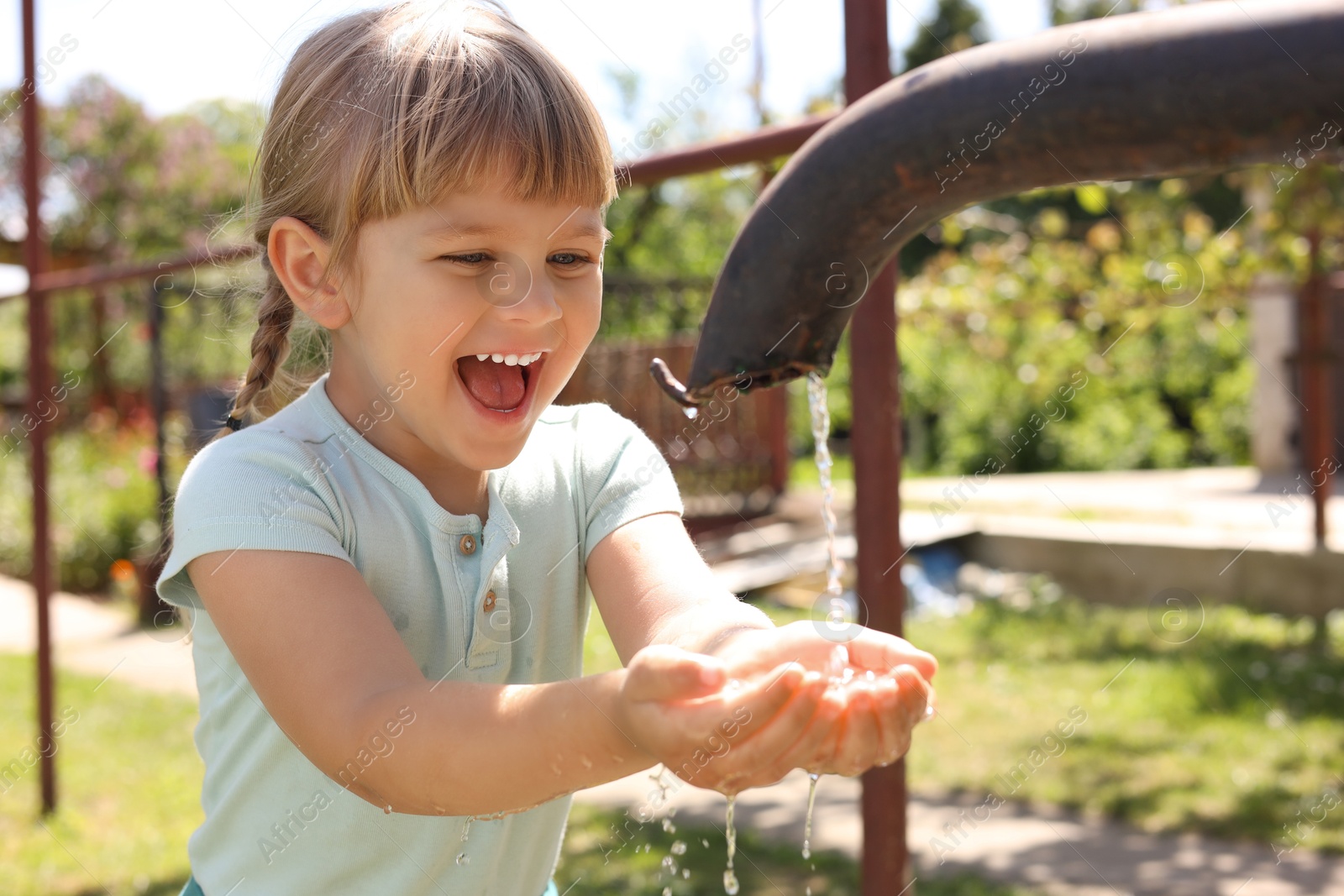 Photo of Water scarcity. Cute little girl drawing water with hands from tap outdoors