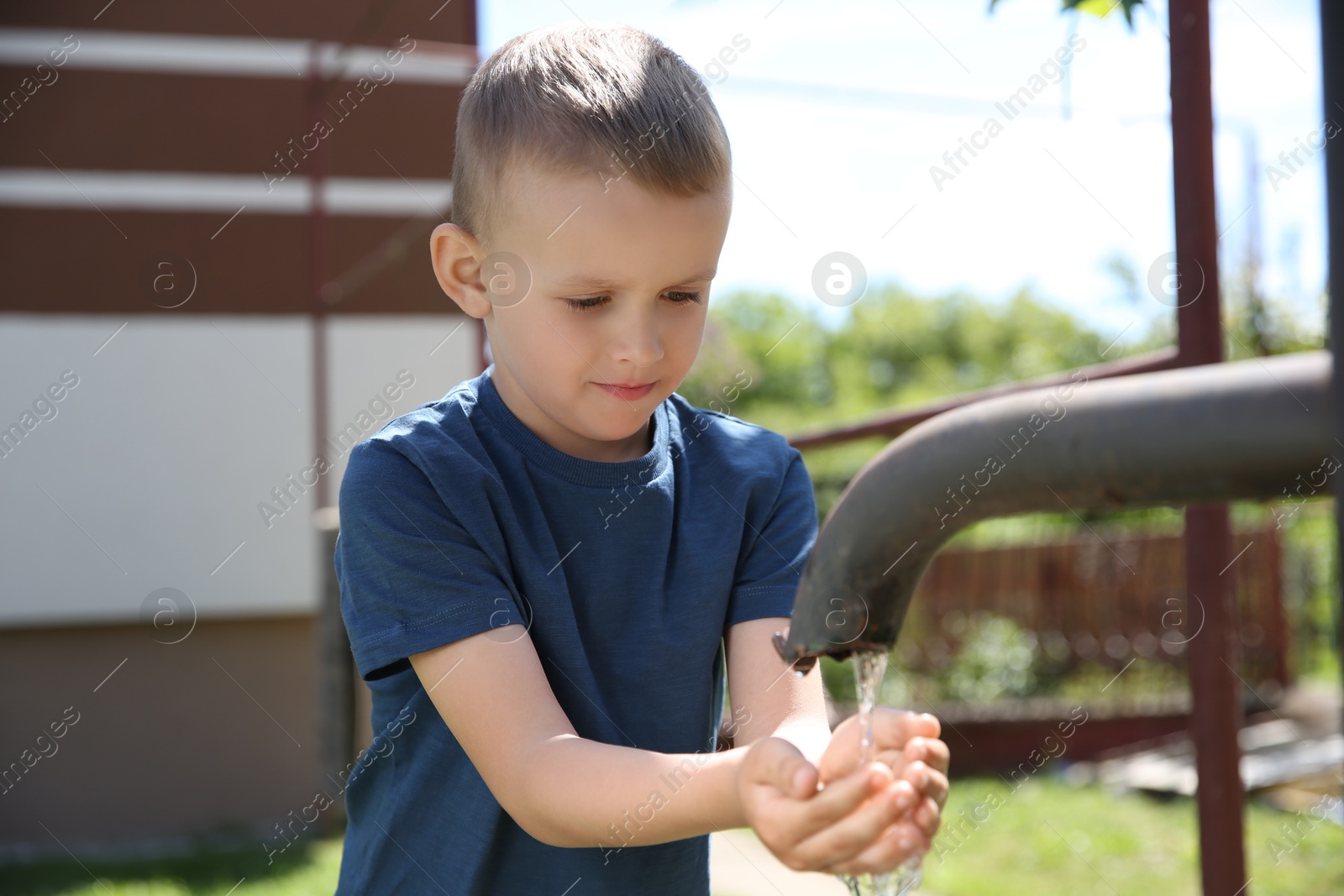 Photo of Water scarcity. Cute little boy drawing water with hands from tap outdoors