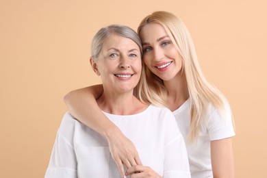 Family portrait of young woman and her mother on beige background