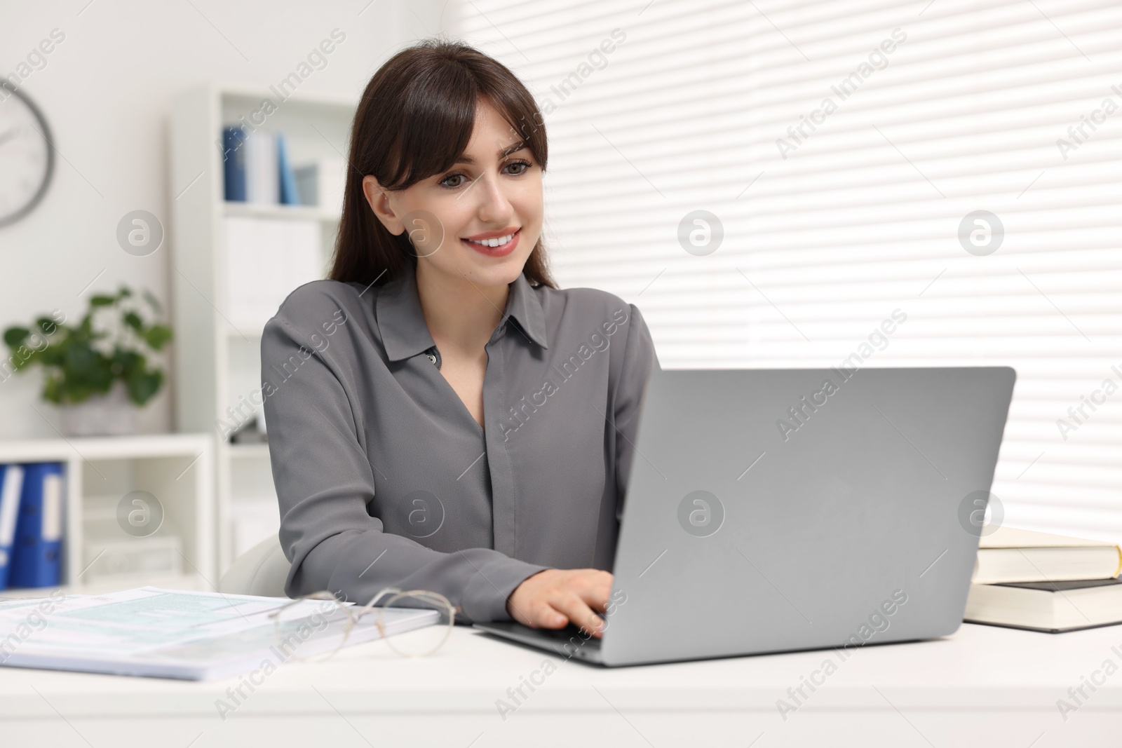 Photo of Smiling secretary working with laptop at table in office