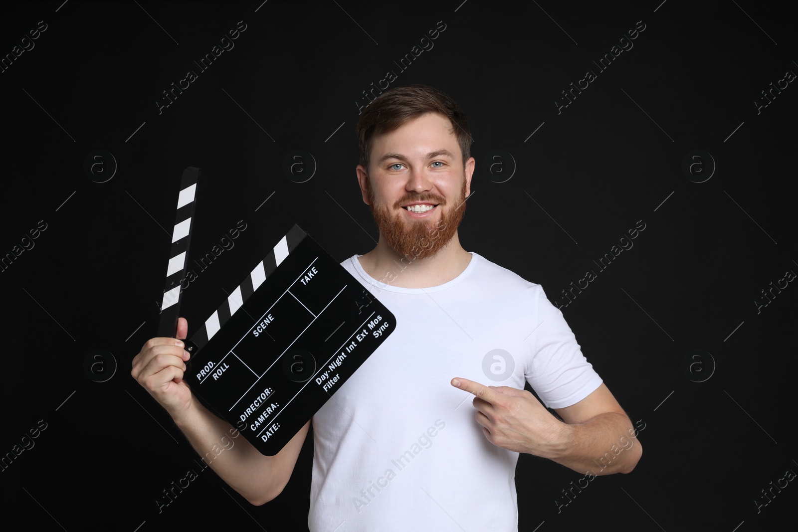 Photo of Making movie. Smiling man pointing at clapperboard on black background