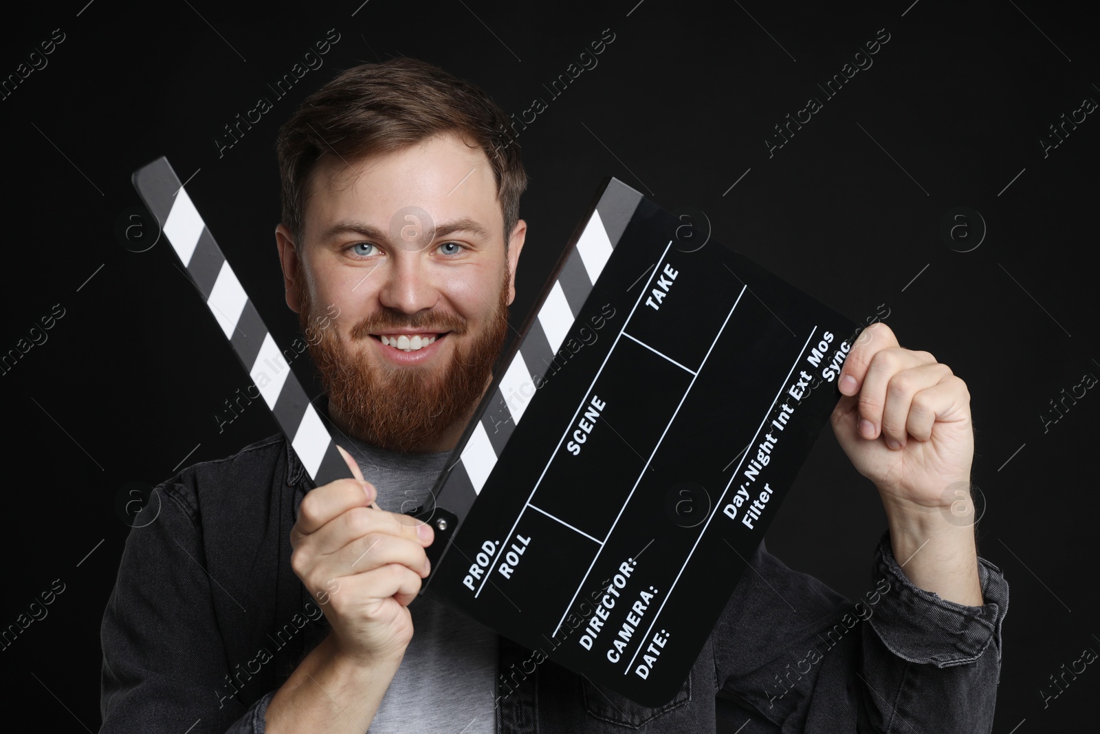 Photo of Making movie. Smiling man with clapperboard on black background