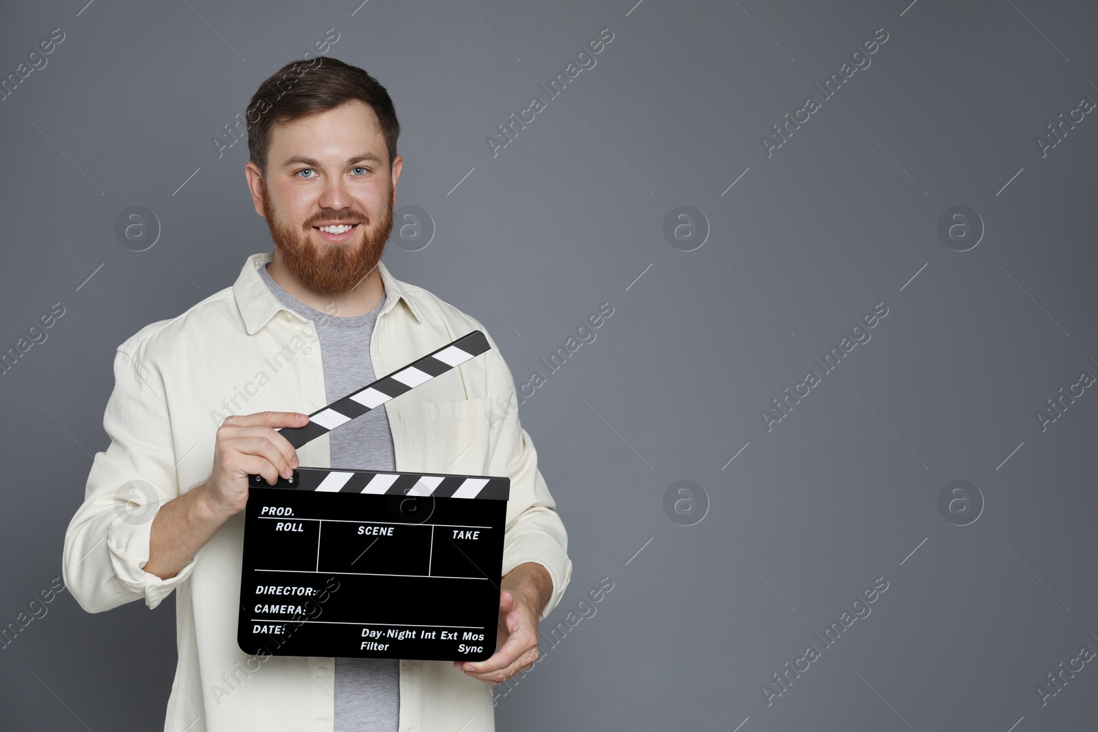 Photo of Making movie. Smiling man with clapperboard on grey background. Space for text