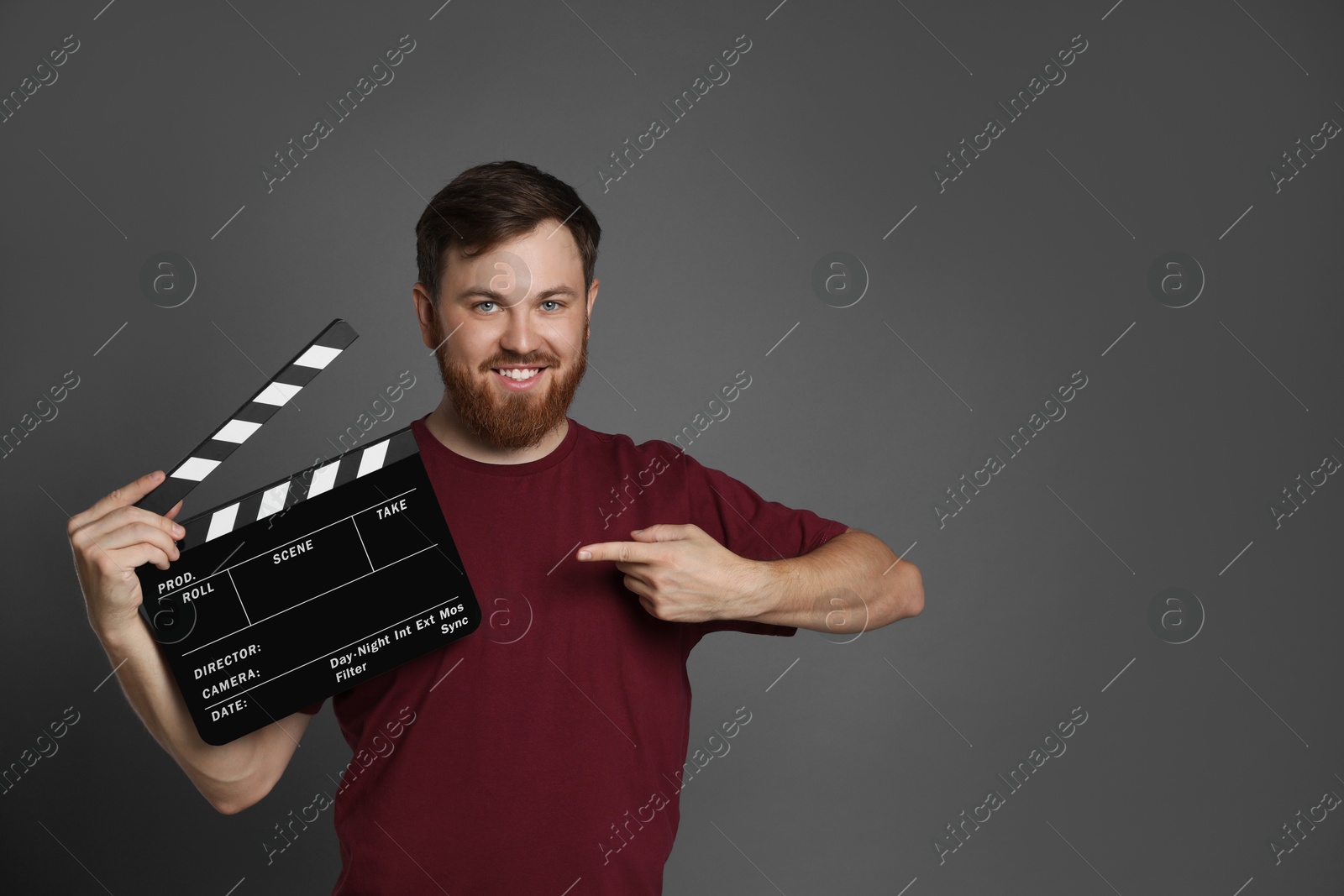 Photo of Making movie. Smiling man pointing at clapperboard on grey background. Space for text