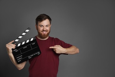 Making movie. Smiling man pointing at clapperboard on grey background. Space for text