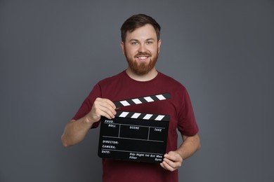 Making movie. Smiling man with clapperboard on grey background