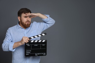 Making movie. Man with clapperboard looking far away on grey background. Space for text