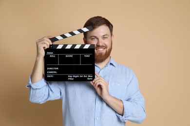 Photo of Making movie. Smiling man with clapperboard on beige background