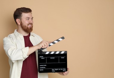 Photo of Making movie. Smiling man with clapperboard on beige background. Space for text
