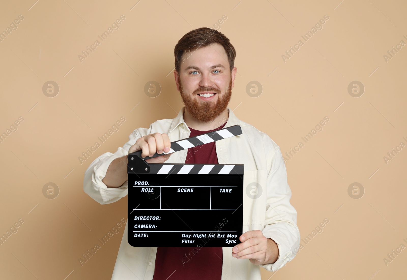 Photo of Making movie. Smiling man with clapperboard on beige background