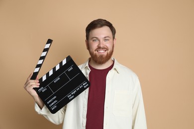 Photo of Making movie. Smiling man with clapperboard on beige background