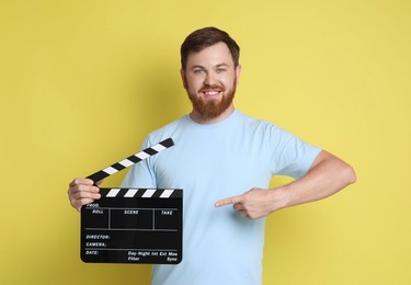 Photo of Making movie. Smiling man pointing at clapperboard on yellow background