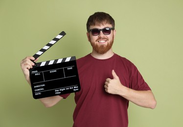 Making movie. Smiling man in sunglasses with clapperboard showing thumb up on green background