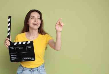 Photo of Making movie. Smiling woman with clapperboard pointing at something on green background. Space for text
