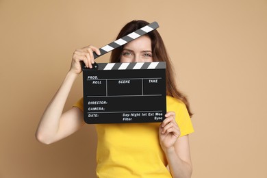 Making movie. Woman with clapperboard on beige background