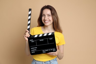 Photo of Making movie. Smiling woman with clapperboard on beige background