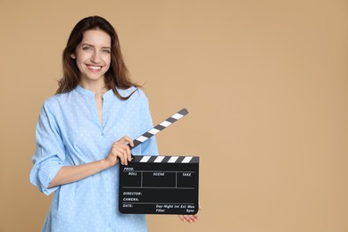 Photo of Making movie. Smiling woman with clapperboard on beige background. Space for text