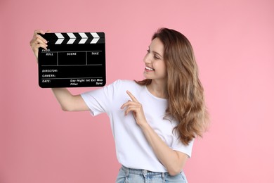 Making movie. Smiling woman pointing at clapperboard on pink background