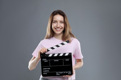 Making movie. Smiling woman with clapperboard on grey background