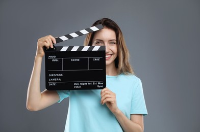Making movie. Smiling woman with clapperboard on grey background