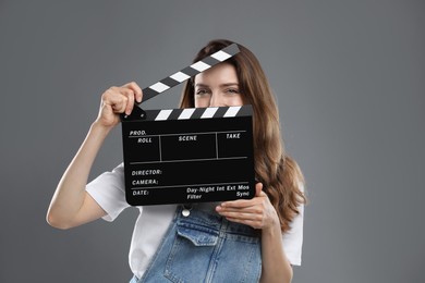 Making movie. Woman with clapperboard on grey background