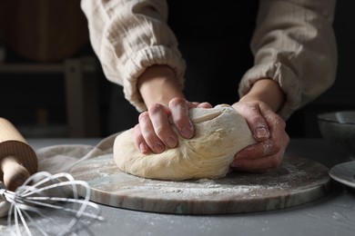 Woman kneading dough at grey table, closeup