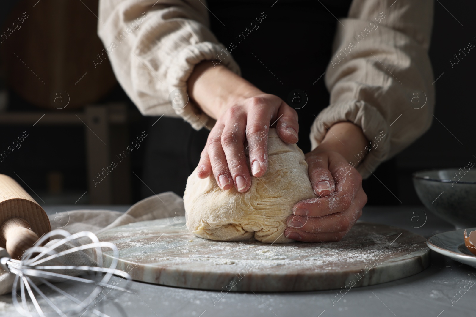 Photo of Woman kneading dough at grey table, closeup