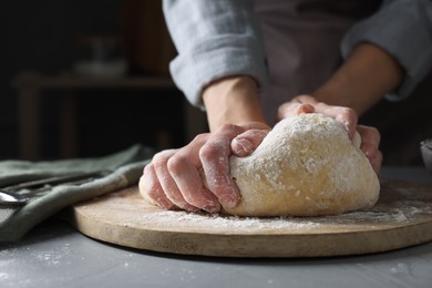 Woman kneading dough at grey table, closeup