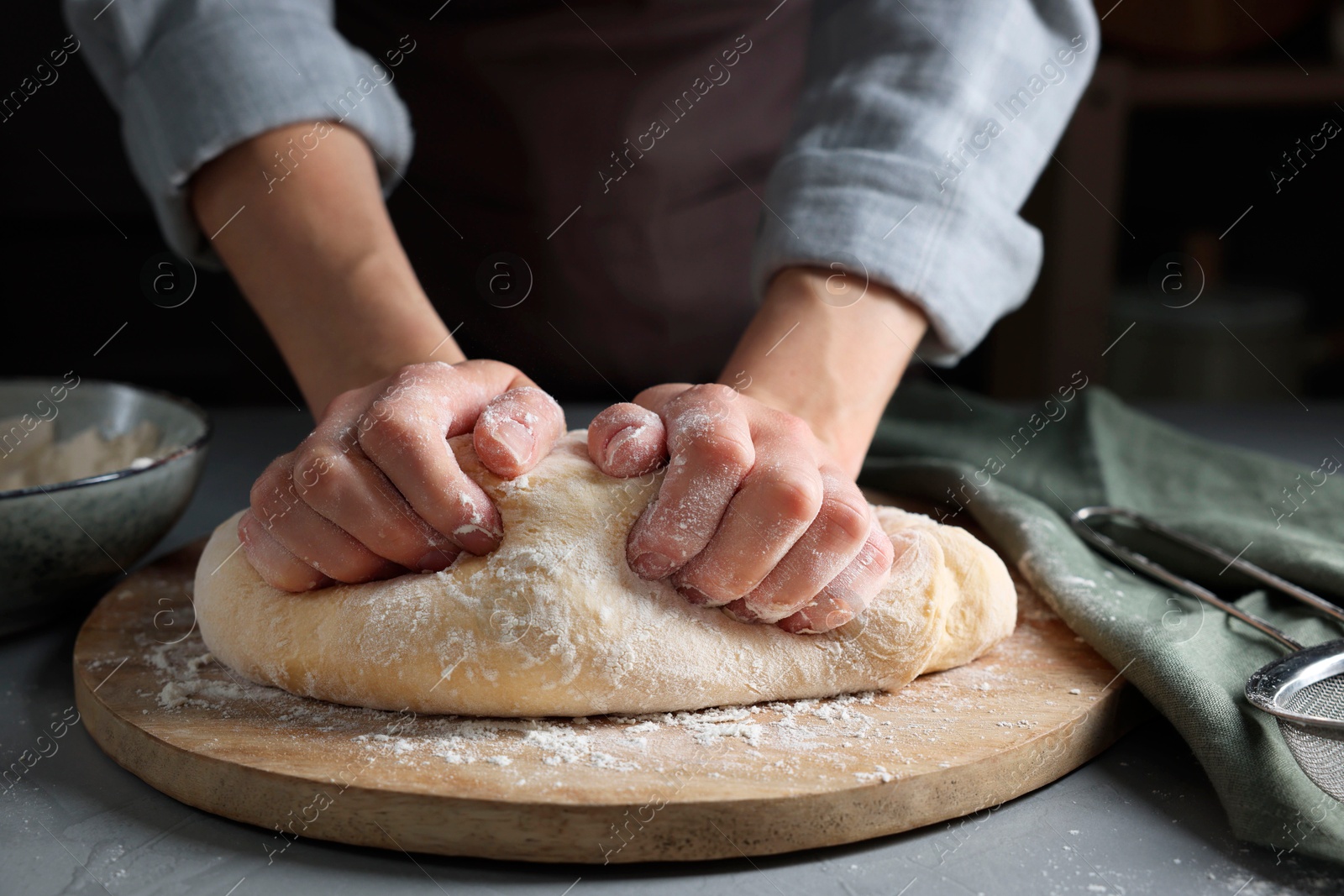 Photo of Woman kneading dough at grey table, closeup