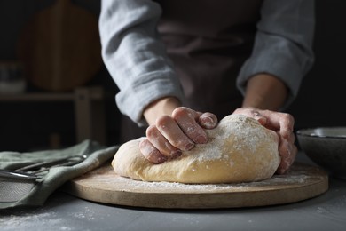 Photo of Woman kneading dough at grey table, closeup