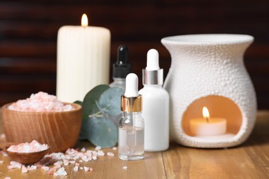 Photo of Different aromatherapy products, burning candles and eucalyptus leaves on wooden table