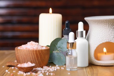 Photo of Different aromatherapy products, burning candles and eucalyptus leaves on wooden table, closeup