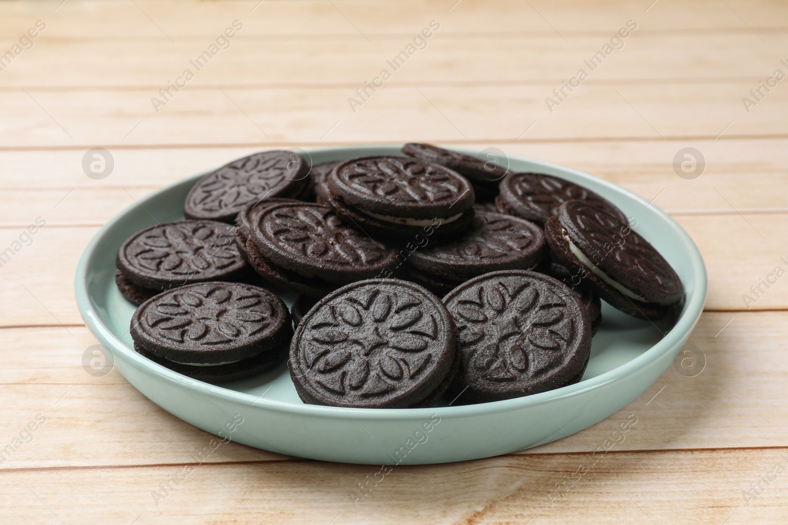 Photo of Plate with tasty sandwich cookies on light wooden table, closeup