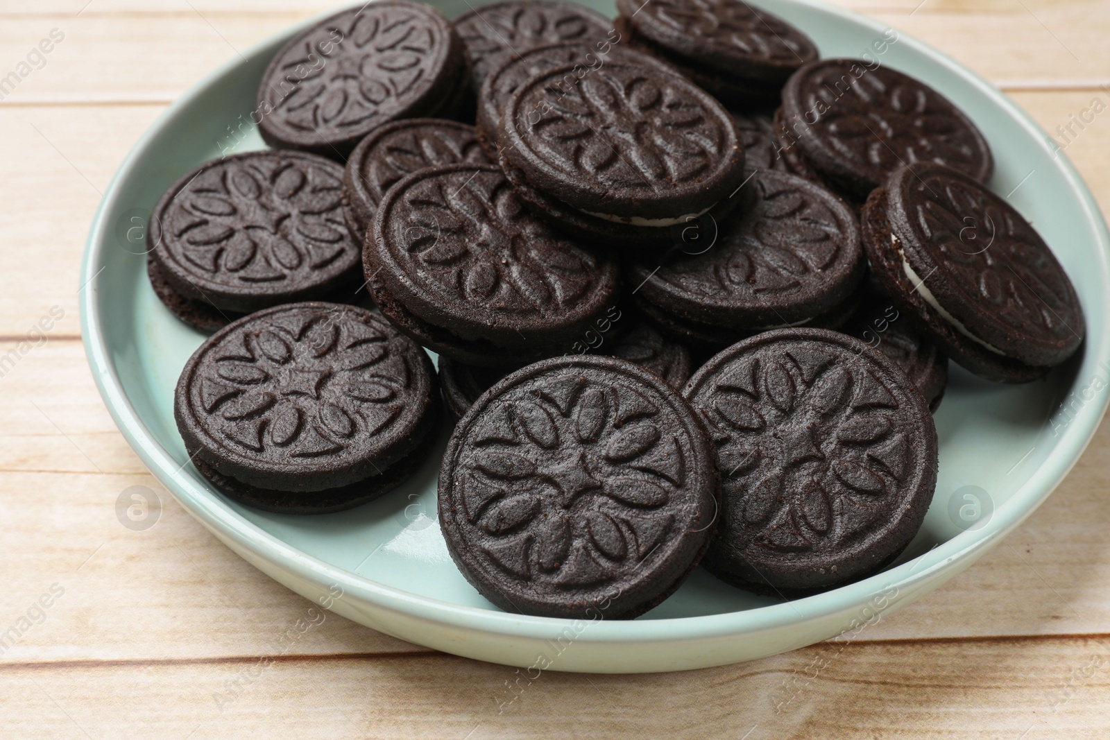 Photo of Plate with tasty sandwich cookies on light wooden table, closeup