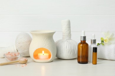 Different aromatherapy products and burning candle on white table