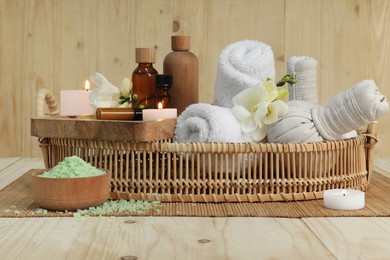 Photo of Aromatherapy products and burning candles in wicker basket on wooden table