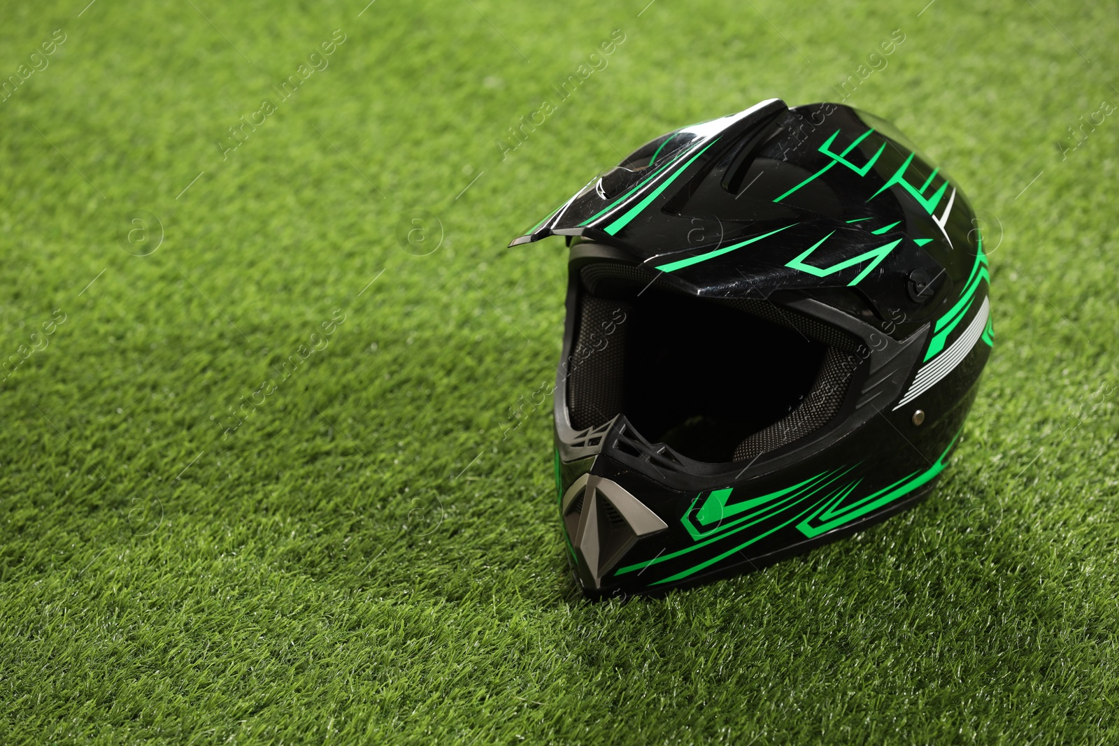 Photo of Modern motorcycle helmet with visor on green grass, space for text