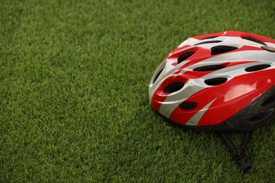 Colorful protective helmet on green grass, space for text