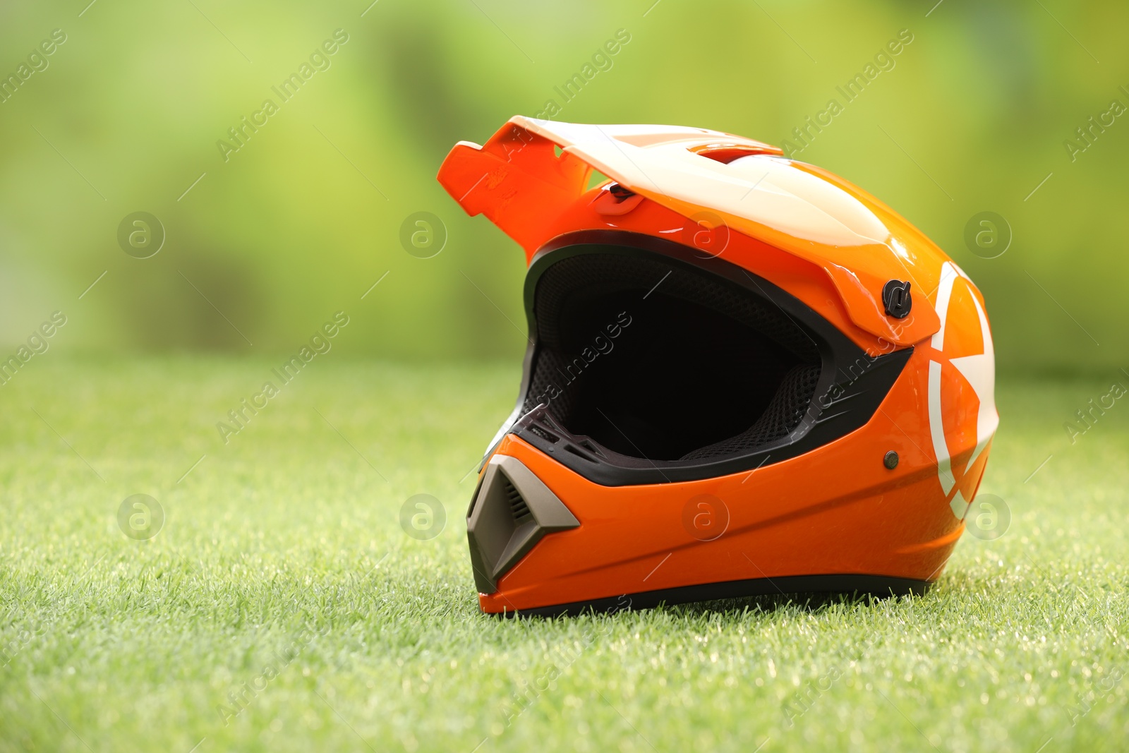 Photo of Orange motorcycle helmet with visor on green grass, space for text